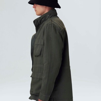 Modelo de perfil com chapéu preto tipo pescador e jaqueta verde-oliva com bolsos grandes.