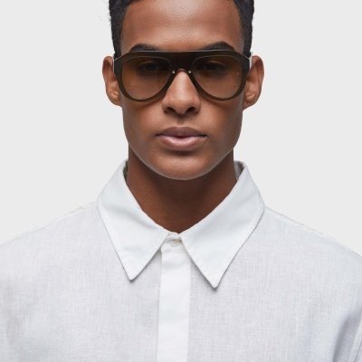 Pessoa com óculos de sol castanhos e camisa branca num fundo cinza claro