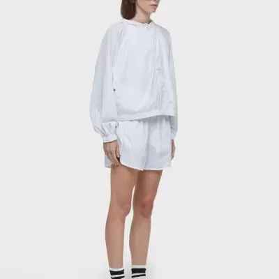 Mulher com conjunto branco de blusa com capuz e calções, óculos escuros castanhos e ténis brancos.