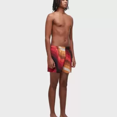 Homem jovem com boxers curtos coloridos e sandálias castanhas.