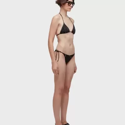 Mulher com biquíni preto com padrão branco e sapatos pretos de malha