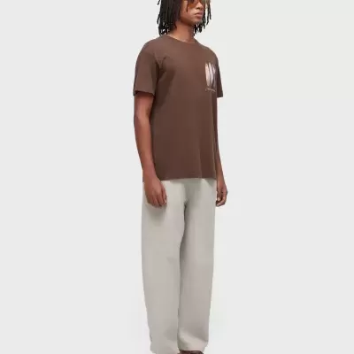 Modelo com t-shirt castanha, calças bege largas e sandálias castanhas