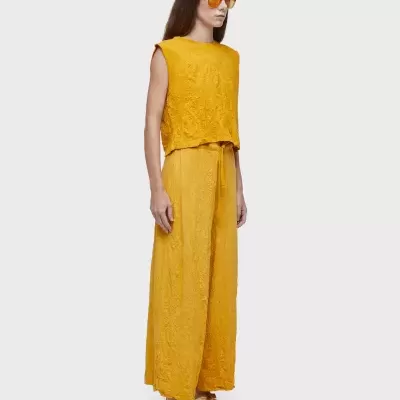 Conjunto amarelo mostarda com top e calças largas, óculos de sol amarelos e sandálias multicoloridas