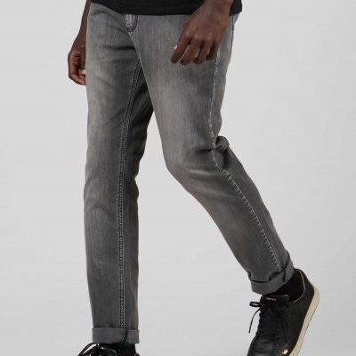 Homem a usar calças de ganga cinzento claro e ténis pretos com sola clara