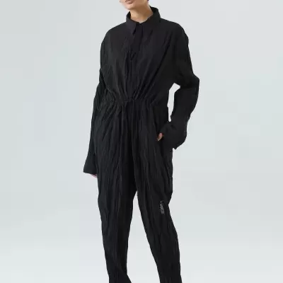 Mulher a usar macacão preto texturizado com cintura ajustável e sapatos pretos