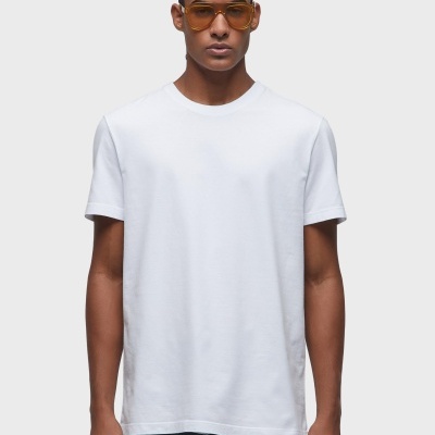 Homem vestindo camiseta branca simples e óculos de sol amarelos, fundo cinza claro.