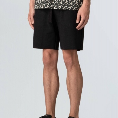 Calções pretos lisos usados por um homem com ténis pretos e top preto floral