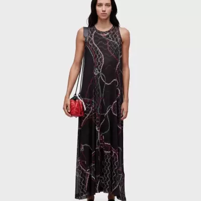 Mulher a usar vestido comprido preto com padrão de correntes e mala vermelha