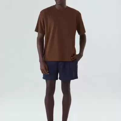 Homem com t-shirt castanha, calções azul escuro e sapatos escuros