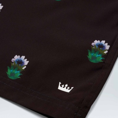 Têxtil escuro com flores azuis e logótipo de coroa branca na bainha