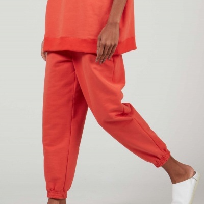 Pessoa vestindo conjunto laranja com chinelos brancos sobre fundo cinza.