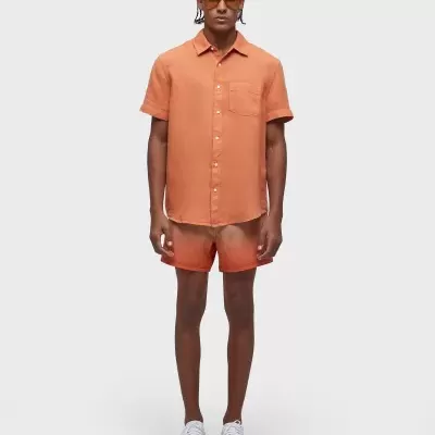 Homem com camisa e calções salmão, sapatos brancos com sola laranja e óculos de sol castanhos