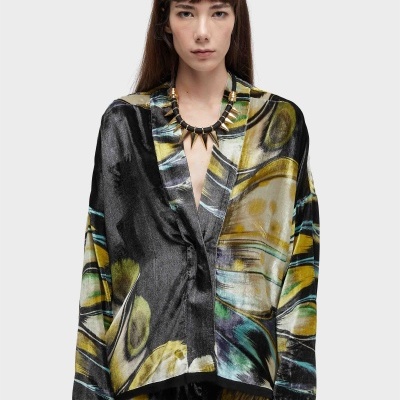 Blazer com padrão abstrato acetinado em várias cores numa modelo com colar de pedras douradas.