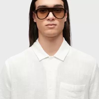 Homem a usar óculos de sol castanhos e camisa branca com bolso