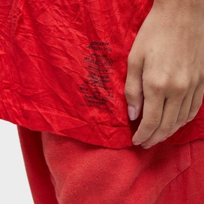 Tecido vermelho com texto e símbolos pretos junto à mão esquerda sobre calças vermelhas de tecido felpudo