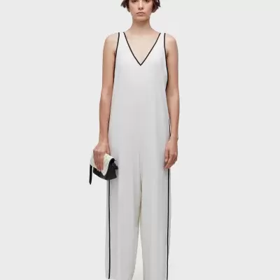 Mulher com macacão branco com detalhes pretos e mala preta com aba branca