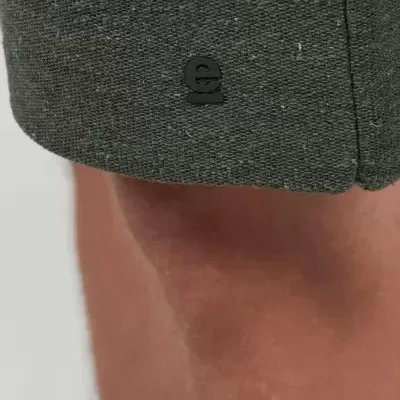 Detalhe de tecido cinza com etiqueta 'e' e pele ao fundo