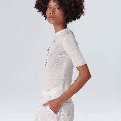 modelo feminino com camisa branca de manga curta e calças brancas em fundo branco