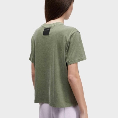 Pessoa de costas com t-shirt verde e calças largas lilás sobre fundo cinzento claro