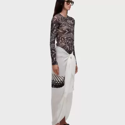 Pessoa com camisa preta transparente de padrão branco, saia branca com estampa preta amarrada e sandálias pretas.