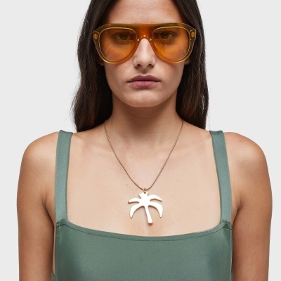 Mulher com óculos de sol âmbar e colar com pendente branco usando top verde