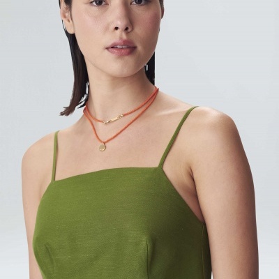 Mulher com vestido verde de alças finas e colares numa parede cinzenta