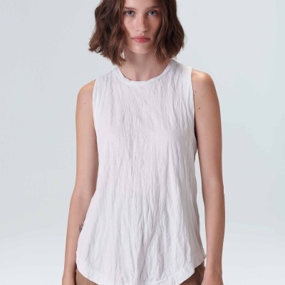 Camisola branca de alças com textura, vestida por mulher, sobre calças castanhas, fundo cinzento