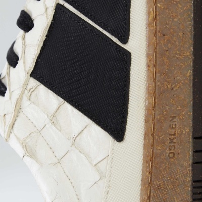 Ténis brancos com detalhes pretos e sola castanha texturizada, com marca OSKLEN