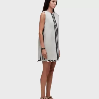 Vestido curto branco com riscas pretas, mulher com sandálias bege, fundo cinza claro