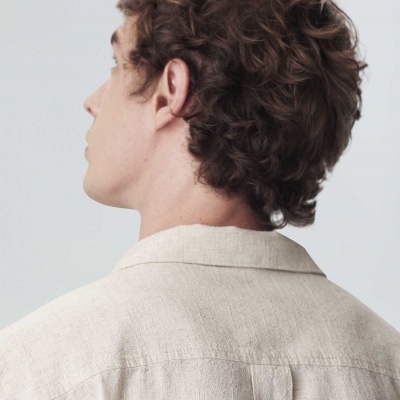 Homem de costas com camisa bege e cabelo encaracolado