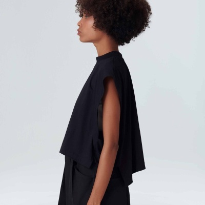 Mulher de perfil com top preto sem mangas e calças pretas em fundo branco