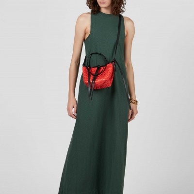 Mulher com vestido verde escuro e mala vermelha em fundo cinza