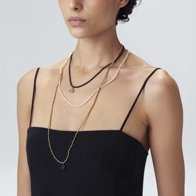 mulher com vestido preto e três colares finos dourado, preto e branco