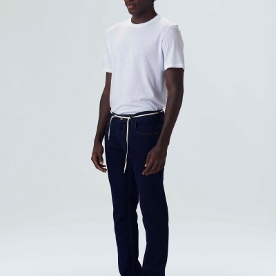 Homem vestindo camisola branca, calças azul-escuras com cordão branco e sapatos brancos em fundo branco