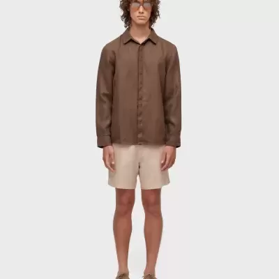 Homem com camisa castanha, calções bege e óculos de sol