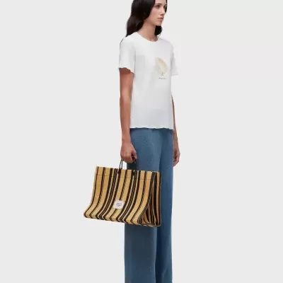 Mulher com t-shirt branca estampada, calças azuis e mala riscada amarela e preta