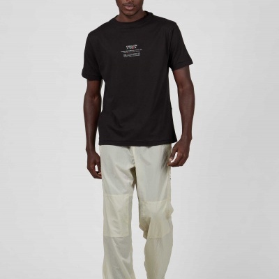 Homem com t-shirt preta com texto branco e calças bege claras em fundo cinza