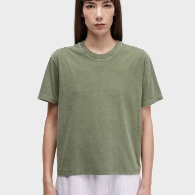 Modelo com t-shirt verde e calças brancas em fundo cinza claro