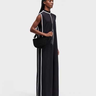 Mulher com vestido comprido preto com riscas brancas e mala preta de ombro