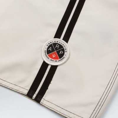 Peça de roupa bege com riscas pretas verticais e emblema redondo colorido com texto