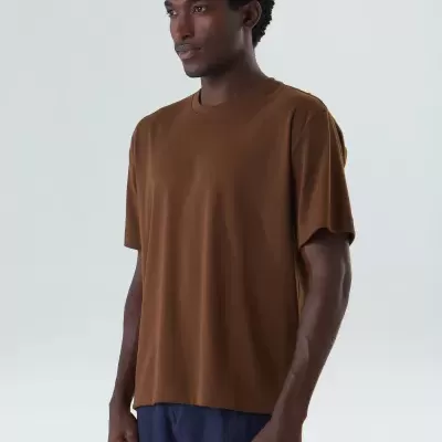 Homem com t-shirt castanha e calções azuis numa fotografia em fundo branco