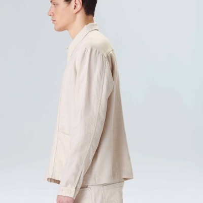 Homem de perfil com camisa e calças bege claro em fundo branco