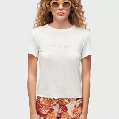 Mulher com t-shirt branca e calções florais coloridos, usando óculos de sol amarelos