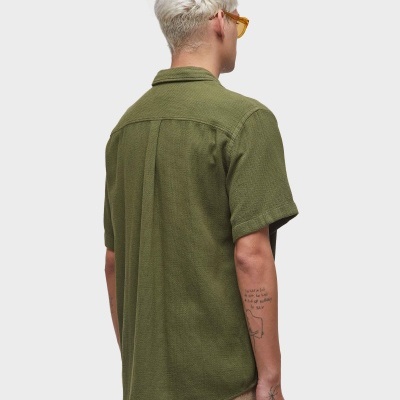 Homem de costas com camisa verde de manga curta e calças bege