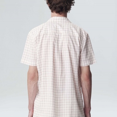 Homem de costas com t-shirt clara de manga curta com padrão de grade e calças claras.