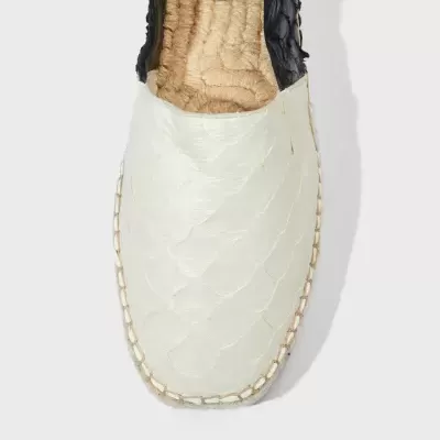 Espadrilha branca e preta com textura de escamas sobre fundo cinza claro