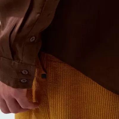 Camisa castanha de manga comprida com botão e calças amarelas texturizadas com riscas verticais