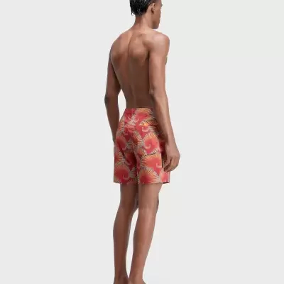 Homem com calções de banho vermelhos com padrão floral, vista traseira.