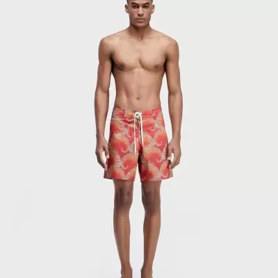 Homem com bermuda de banho vermelha com padrão de espirais amarelas e azuis