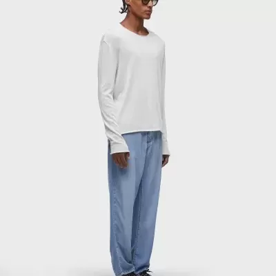 Homem com t-shirt branca de manga comprida, calças azuis largas e sapatilhas cinzentas, fundo branco